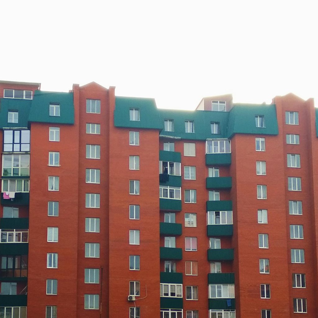 Exterior of modern multistorey apartment building with green roof and balconies on bright day